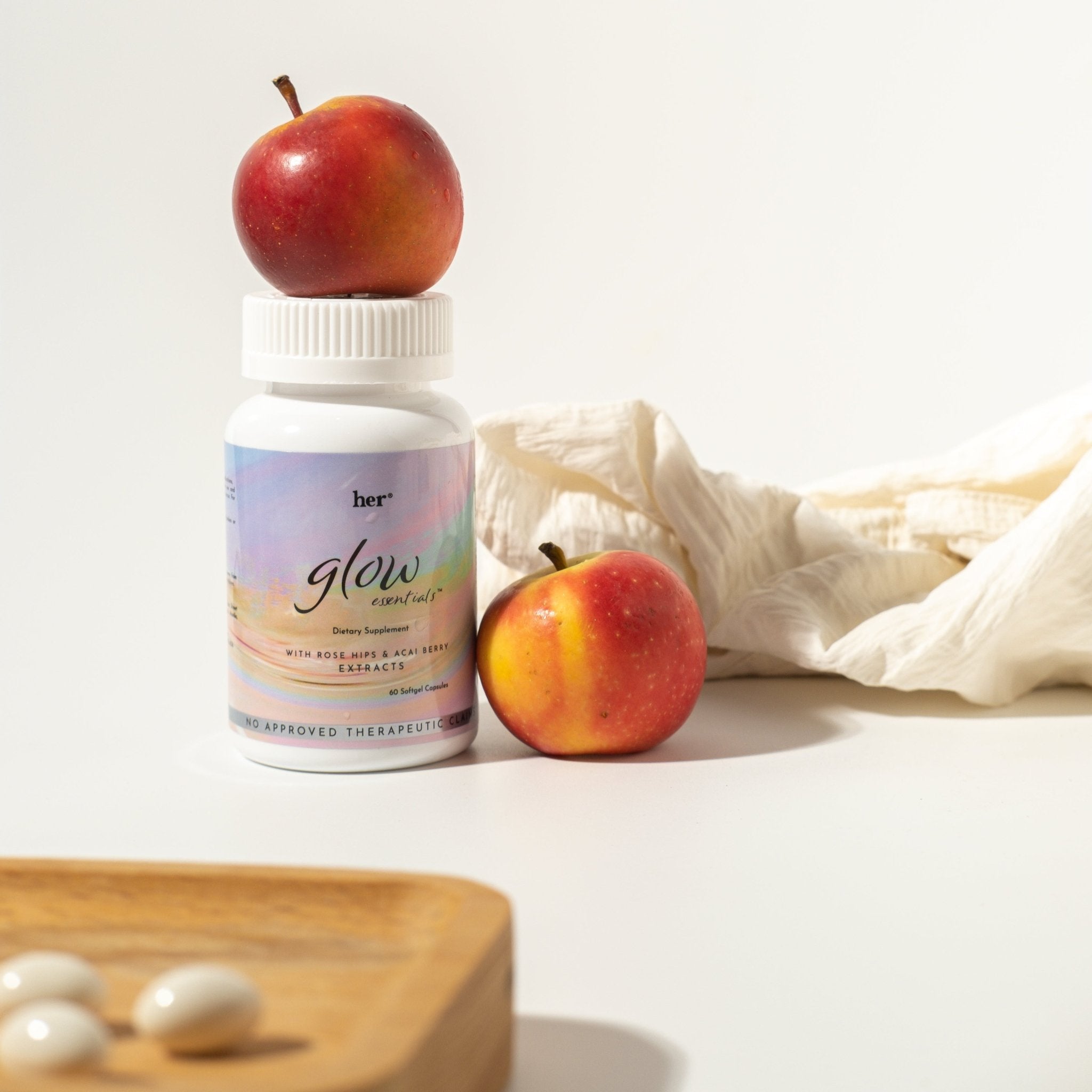 HER® Glow Essentials® bottle next to key ingredients like collagen peptides, hyaluronic acid, and vitamin C, highlighting the formula's focus on foundational health and skin radiance.